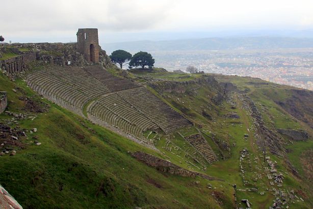 Las magníficas ruinas de un antiguo teatro construido en una empinada ladera en la antigua ciudad de Pérgamo (Bergama), en Esmirna, con el perfil urbano moderno de Bergama al fondo.