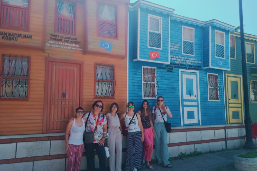 Un grupo de turistas posan juntas frente a coloridos pabellones de madera y letreros culturales en el Barrio Cultural Turco de Estambul.