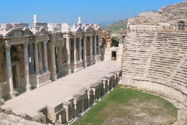 El histórico edificio del escenario, con sus columnas y arcos, del antiguo teatro de Pamukkale en Hierápolis, con filas de asientos de piedra que se elevan a su lado.