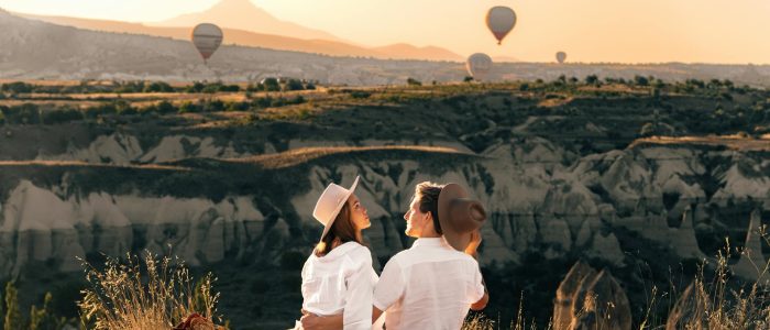 Una pareja romántica contempla el amanecer sobre globos aerostáticos con el paisaje de cuento de hadas del valle de Capadocia de fondo.