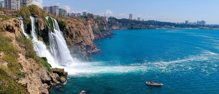 La cascada de Düden, en Antalya, cae en cascada desde altos acantilados hasta las aguas turquesas del Mediterráneo, mientras una pequeña embarcación turística se desliza sobre el mar.