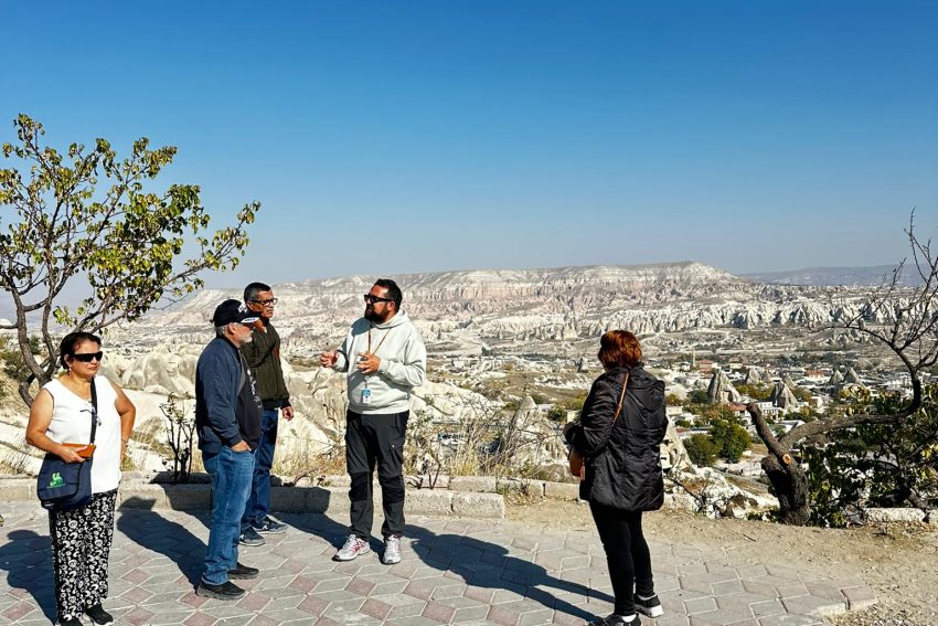 Un momento en el que un guía turístico proporciona información a un grupo de turistas con el magnífico paisaje del valle de Capadocia como telón de fondo.