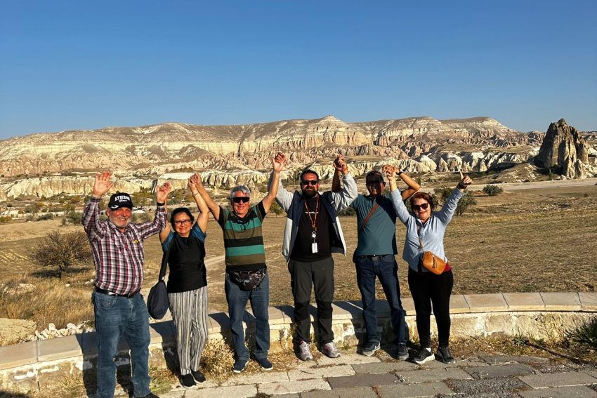 Un grupo de seis amigos posan alegremente con las manos en alto, con el singular paisaje de Capadocia como telón de fondo.