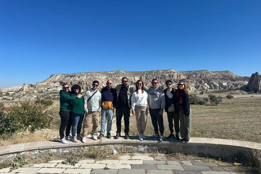 Un grupo de nueve amigos posando juntos con las emblemáticas chimeneas de hadas y el paisaje del valle de Capadocia como telón de fondo.