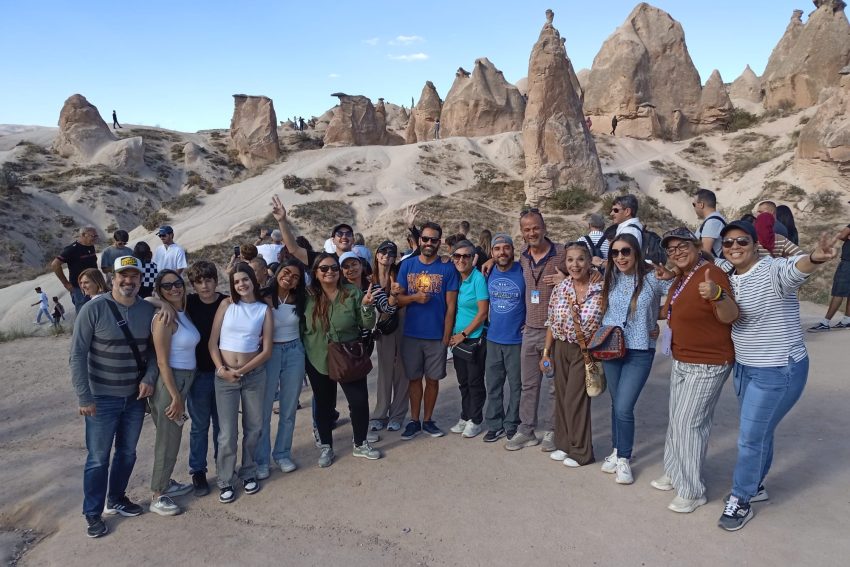 "Un numeroso grupo de turistas posa alegremente frente a las emblemáticas chimeneas de hadas en el valle de Devrent (Valle de los Sueños) en Capadocia."