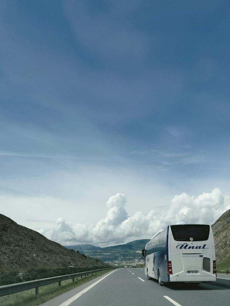 Un autobús moderno circula por una carretera rodeada de majestuosas montañas, creando un paisaje impresionante que evoca la belleza de Turquía. Este trayecto es una opción popular para quienes viajan de Estambul a Capadocia, ofreciendo vistas panorámicas del valle y la naturaleza circundante.